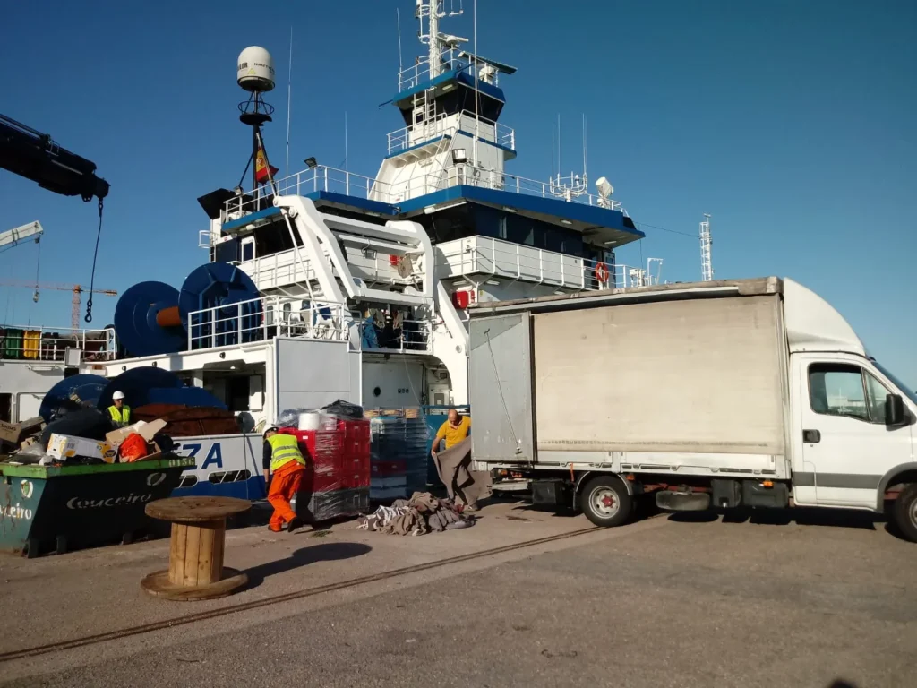 Trabajadores descargando materiales de un camión junto a un barco.