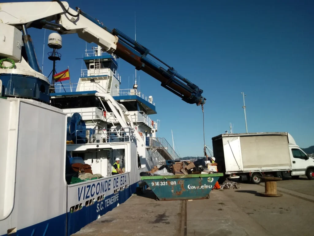 Grúa descargando materiales desde camión hacia el barco "Vizconde de Eza".