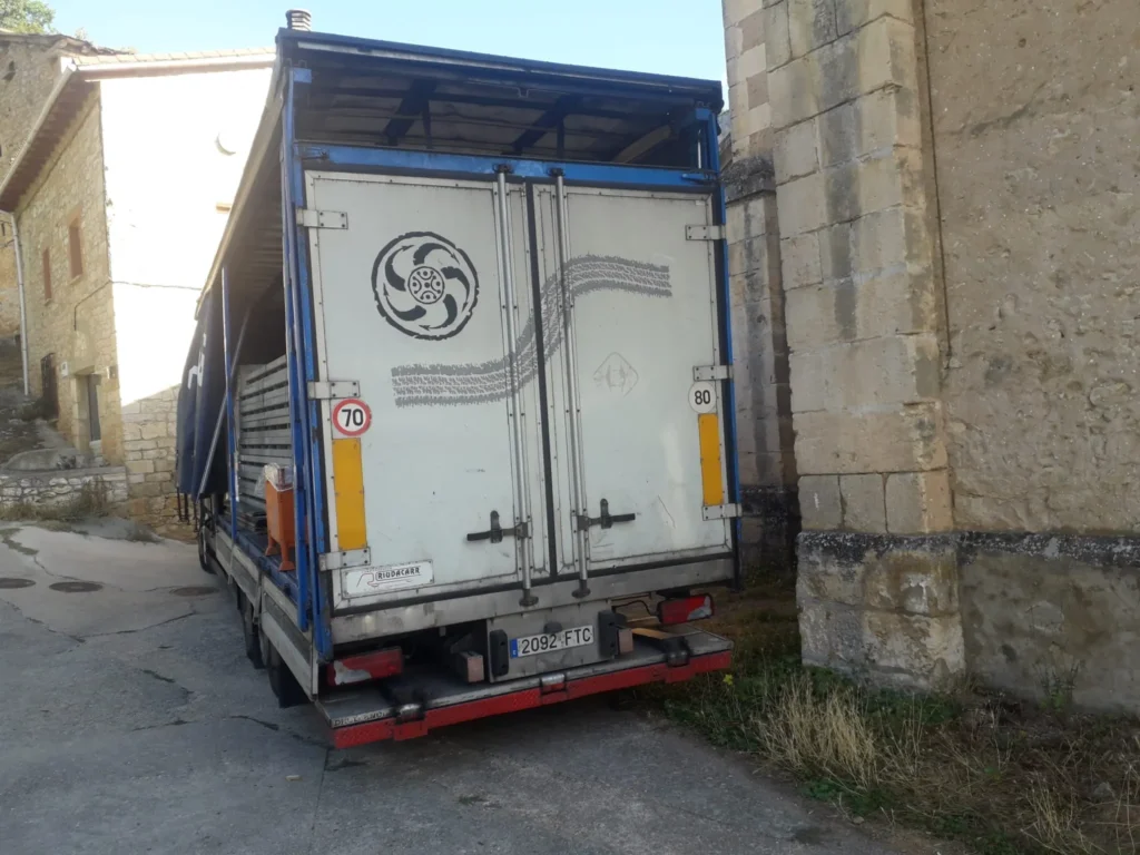 Parte trasera de un camión con puerta abierta junto a un edificio de piedra.