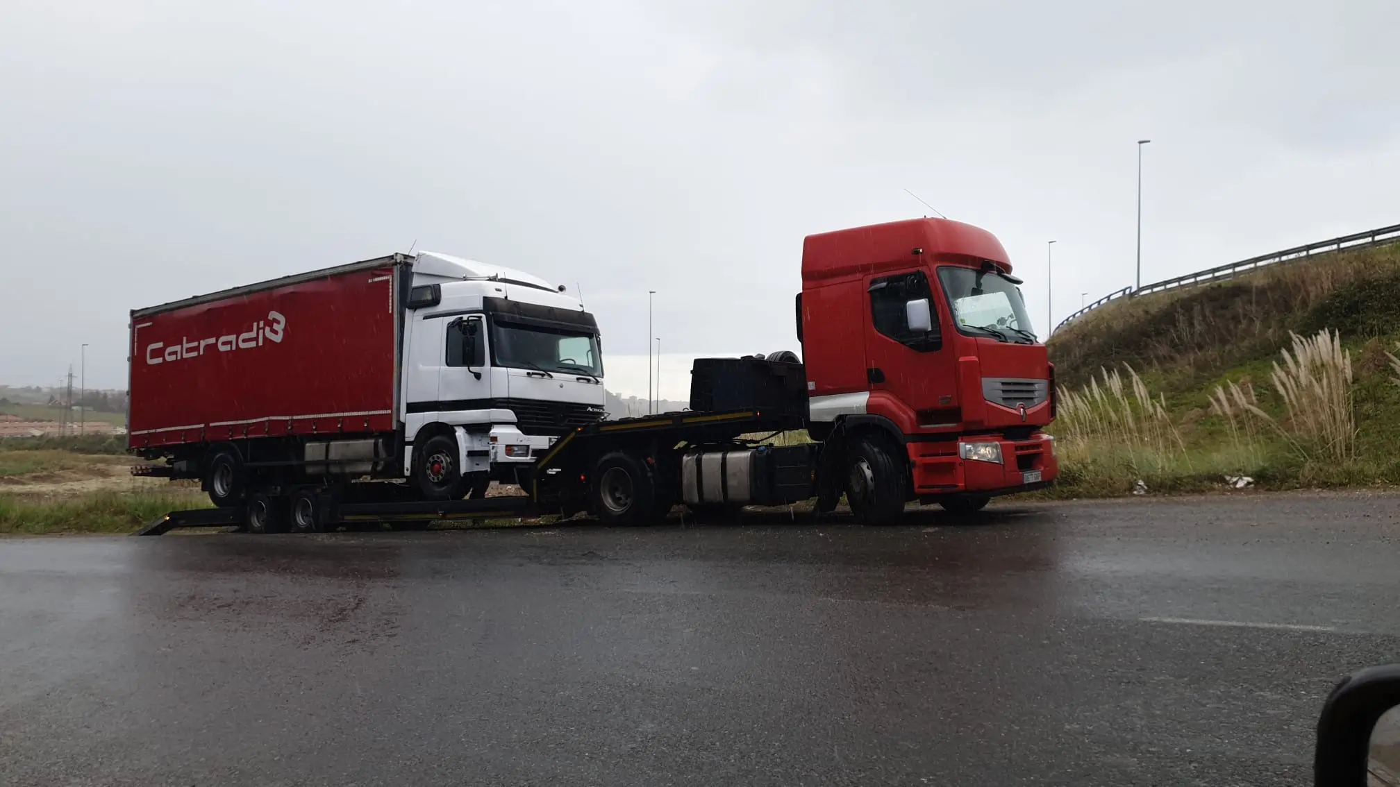 Dos camiones rojos en una carretera bajo lluvia.