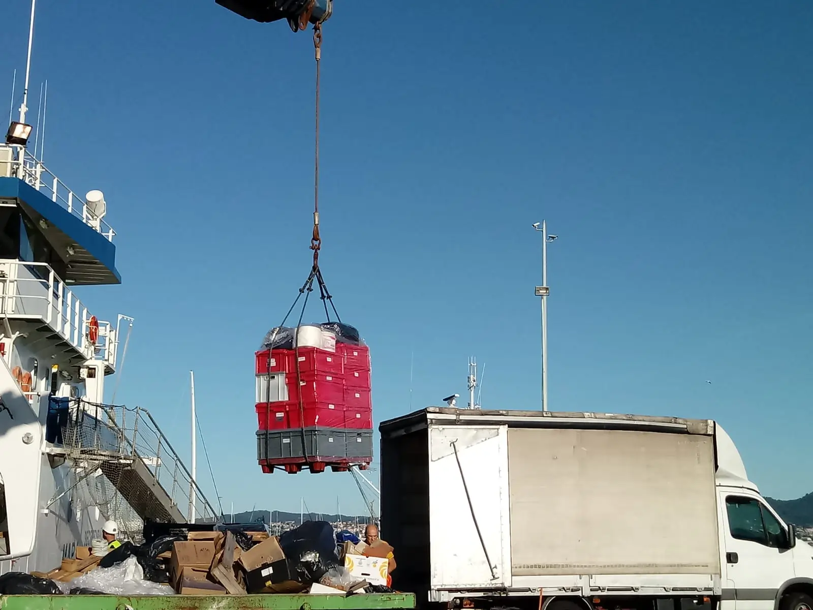 Cargamento siendo elevado con una grúa desde un barco hacia un camión.