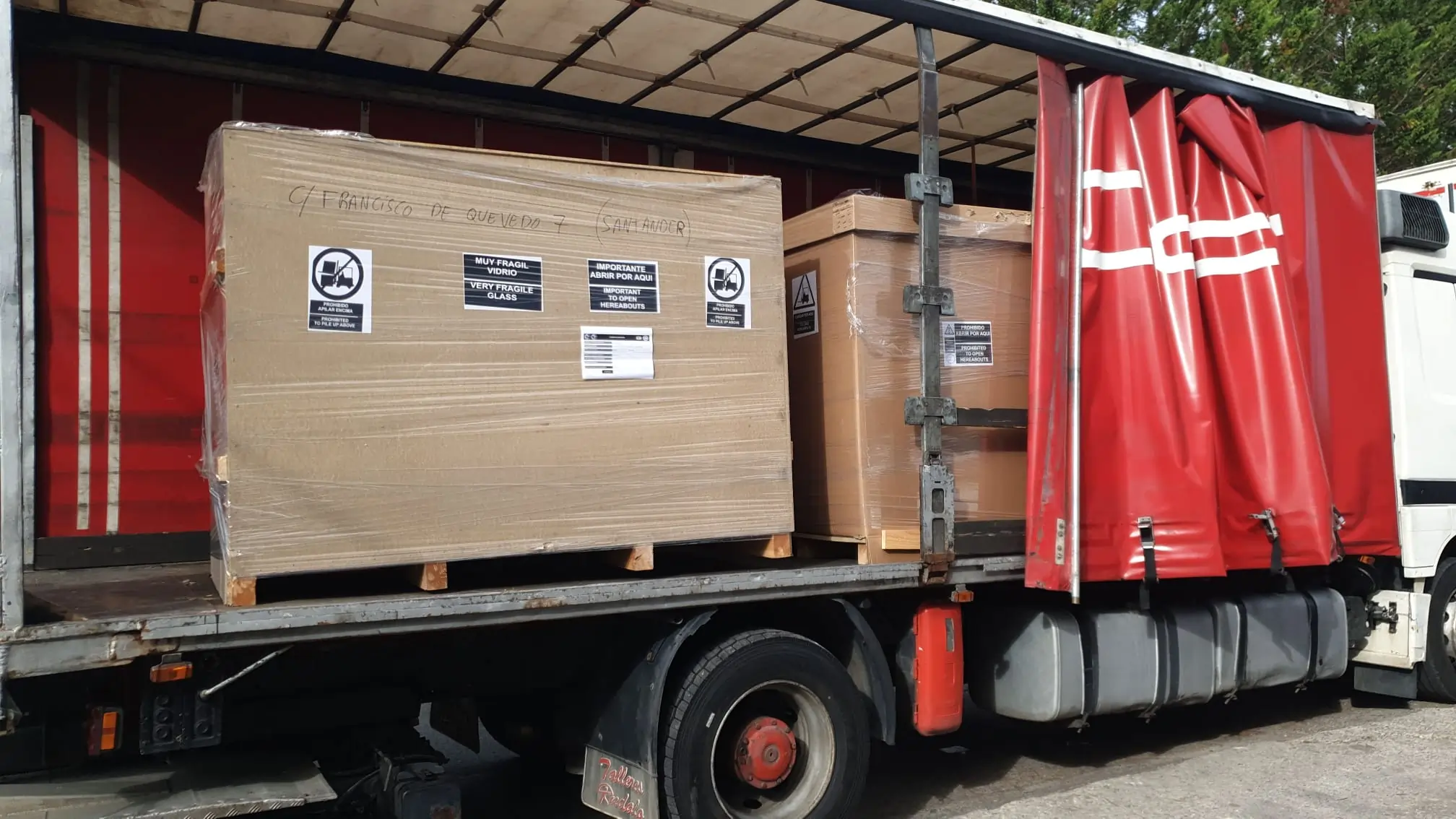 Cajas grandes etiquetadas como frágiles dentro de un camión de lona roja.