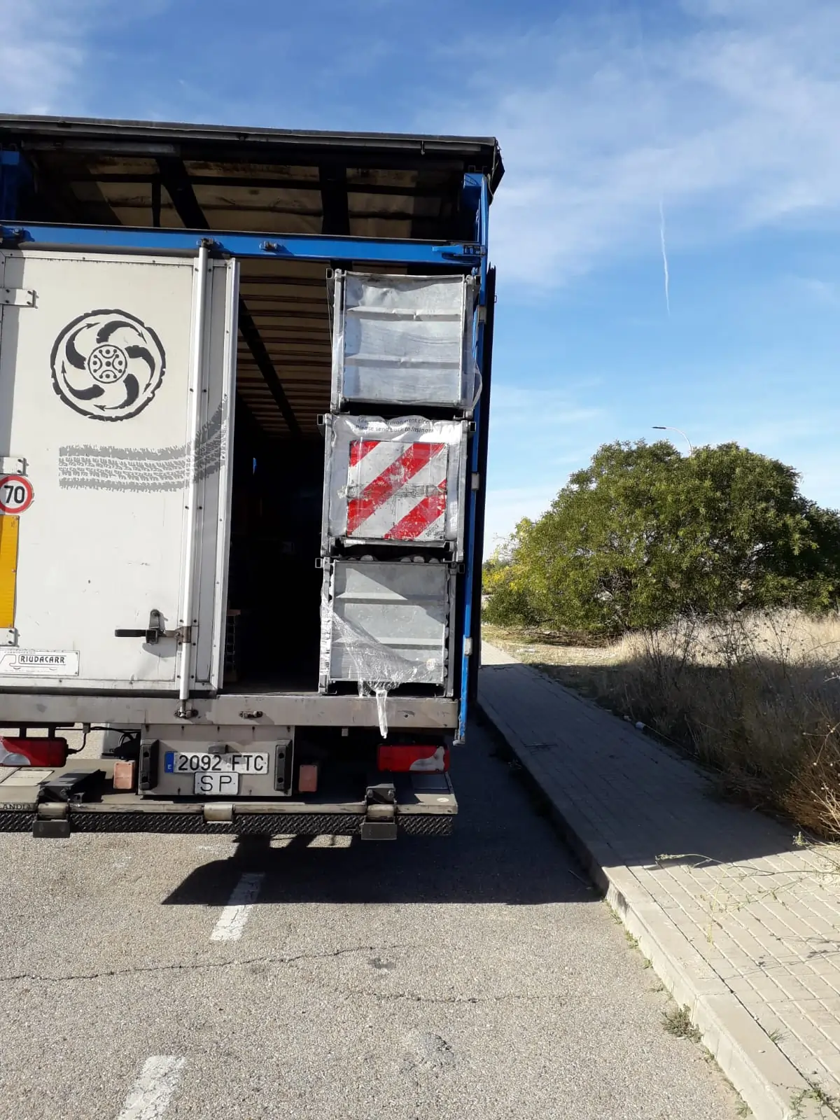 Camión de carga con la puerta trasera abierta estacionado en una calle soleada.
