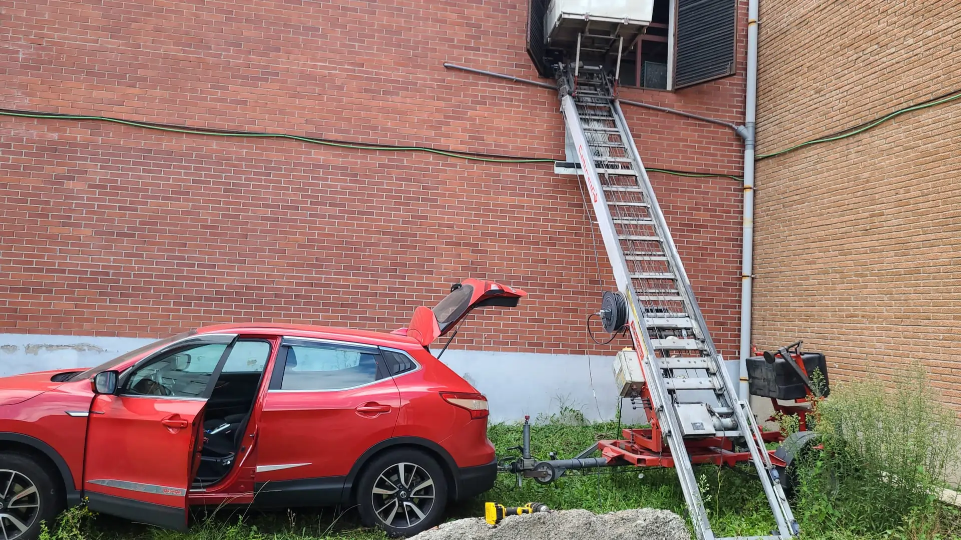 Coche rojo y elevador de mudanzas junto a un edificio de ladrillo.