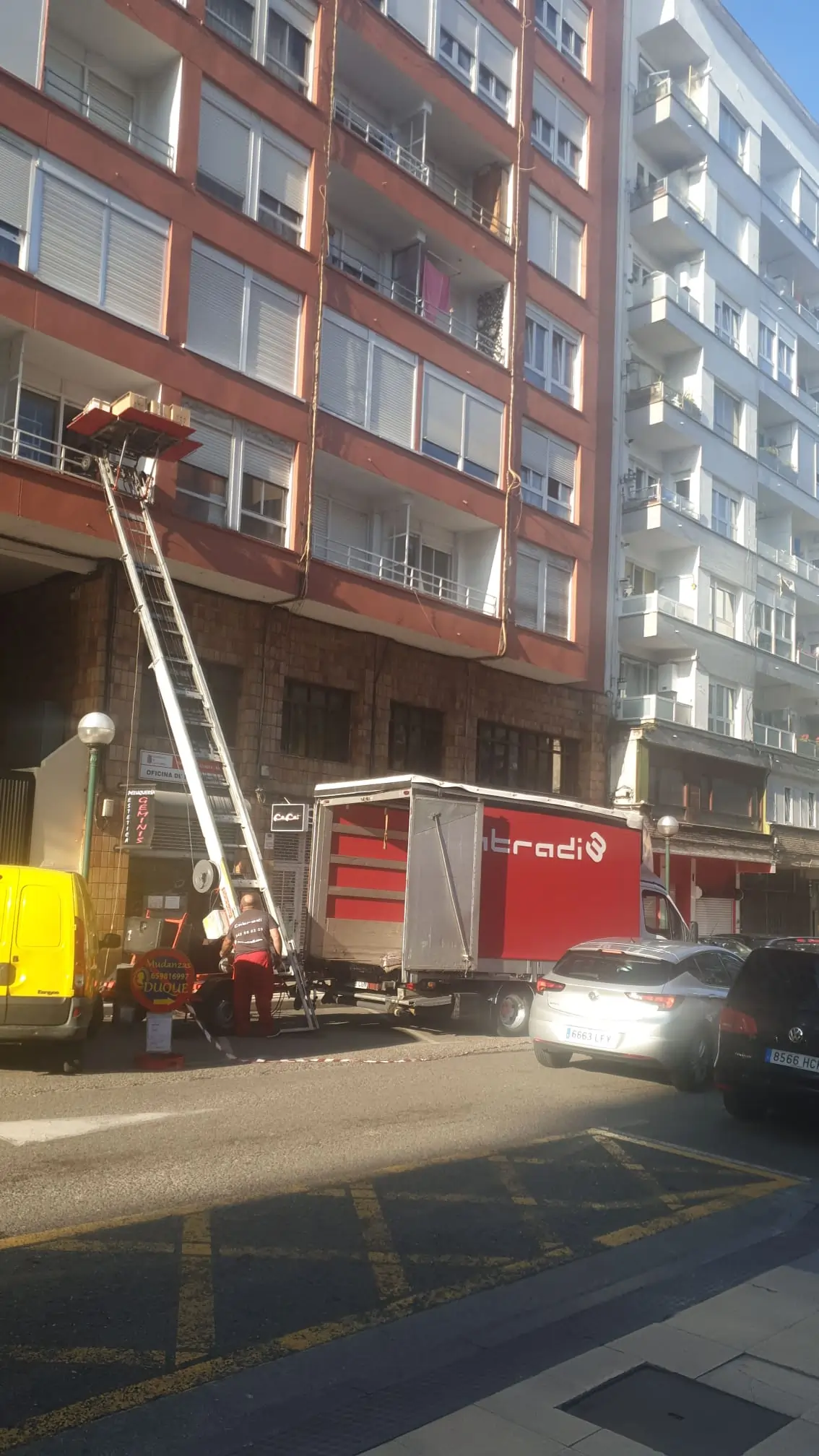 Camión de mudanzas con elevador frente a un edificio de apartamentos.