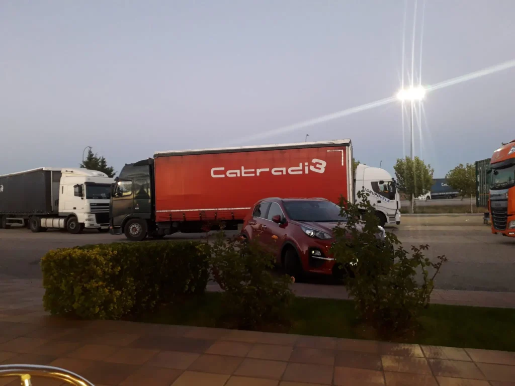 Camiones estacionados junto a un coche rojo en un aparcamiento iluminado.