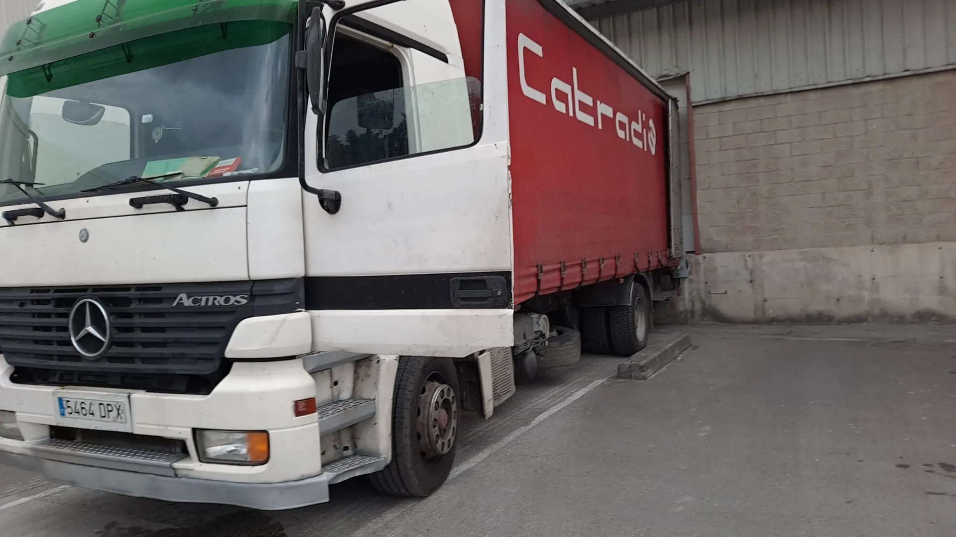 Camión Mercedes-Benz Actros blanco con remolque rojo estacionado junto a un edificio.