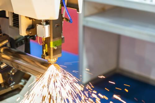 close up nozzle component of high precision cnc plasma laser cutting machine during engrave or perforate workpiece (pipe) and many sparks with automatic feed and rotation "u2013 clamp